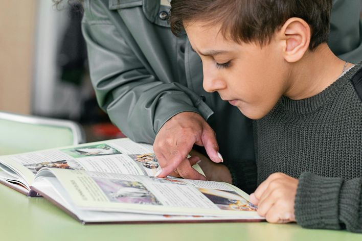 A woman helps a boy read in a classroom setting. Educational support concept.