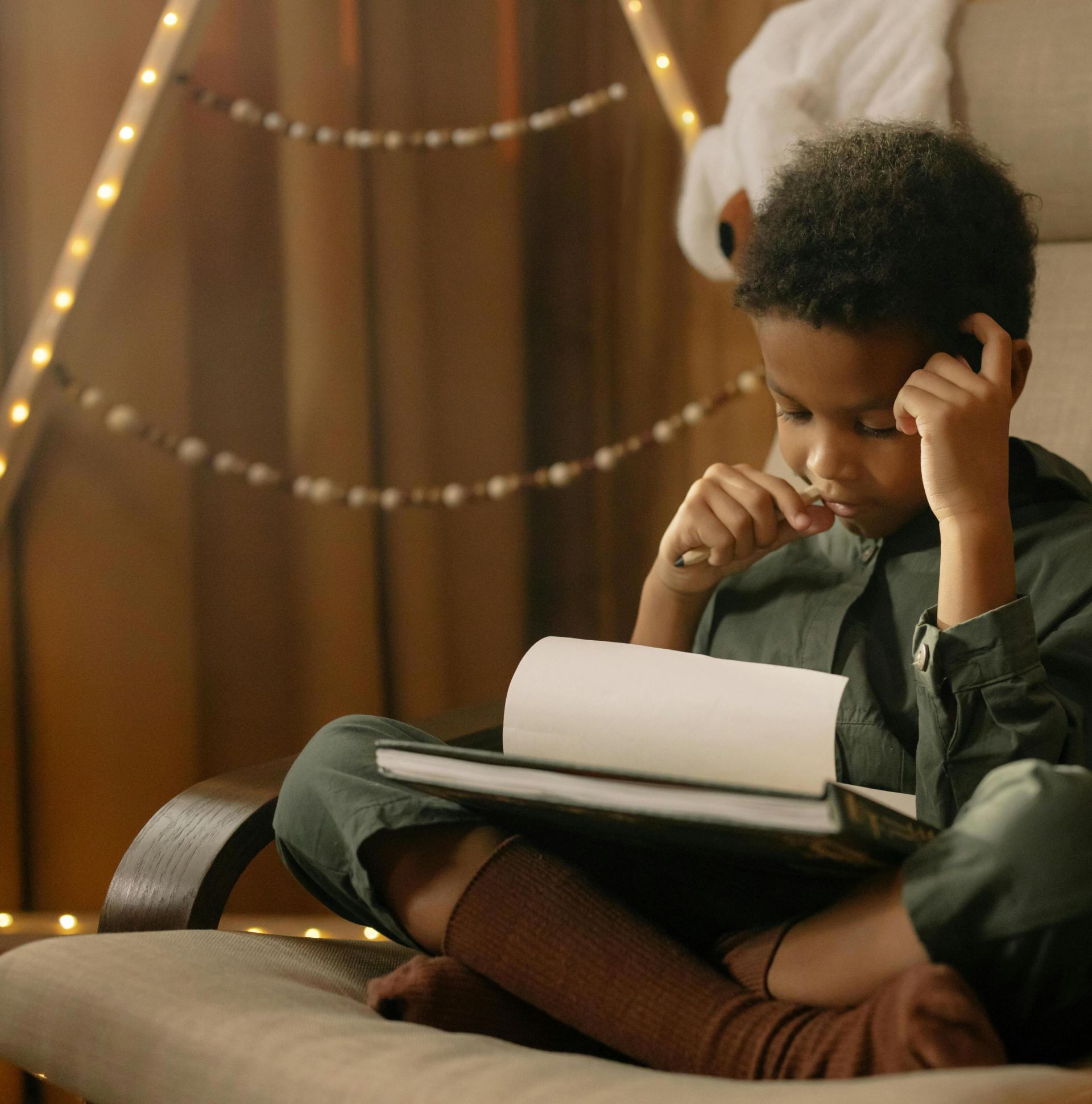 A young child intensely focused on drawing while sitting indoors in a cozy and warm setting.