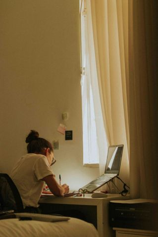 A young woman writing at a desk by a window, bathed in soft light, illustrating concentration.